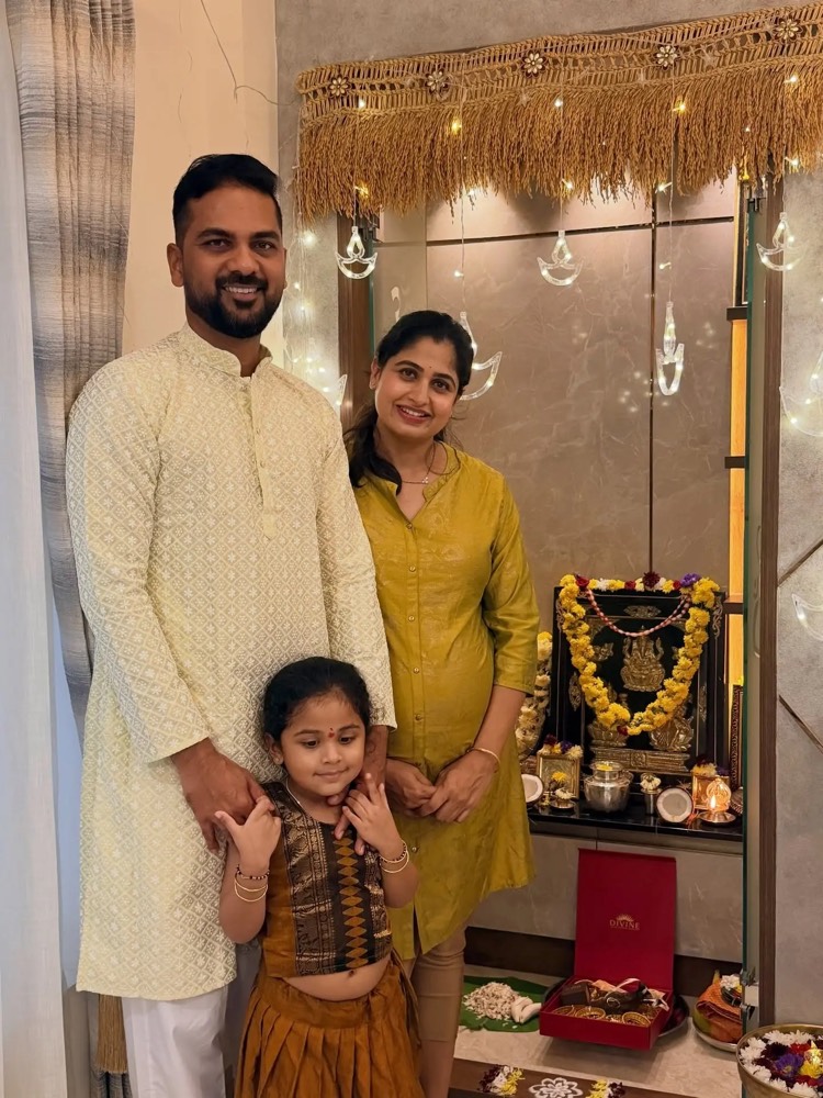 Chaithra Rai in a yellow kurta beside her husband and elder daughter at a decorated home shrine