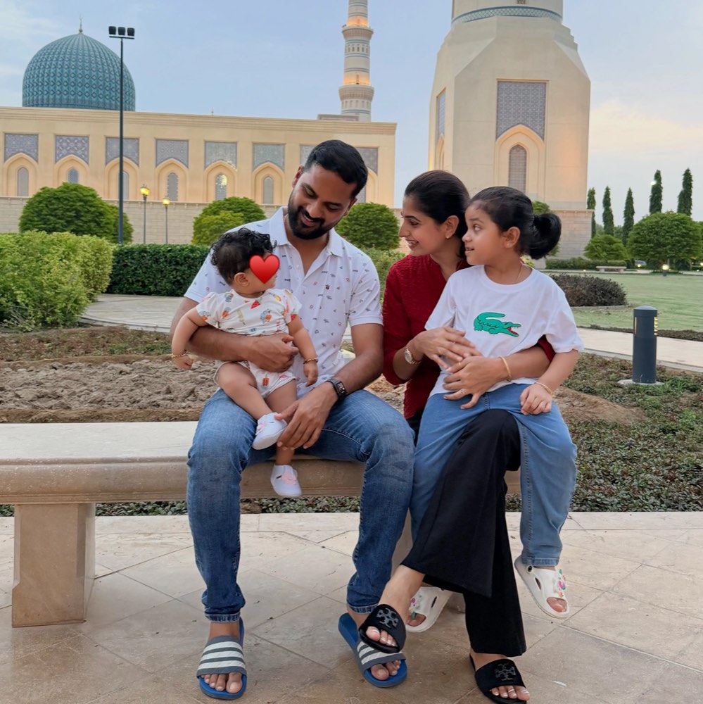 Chaithra Rai and her husband sitting on a bench outside a mosque with their two daughters