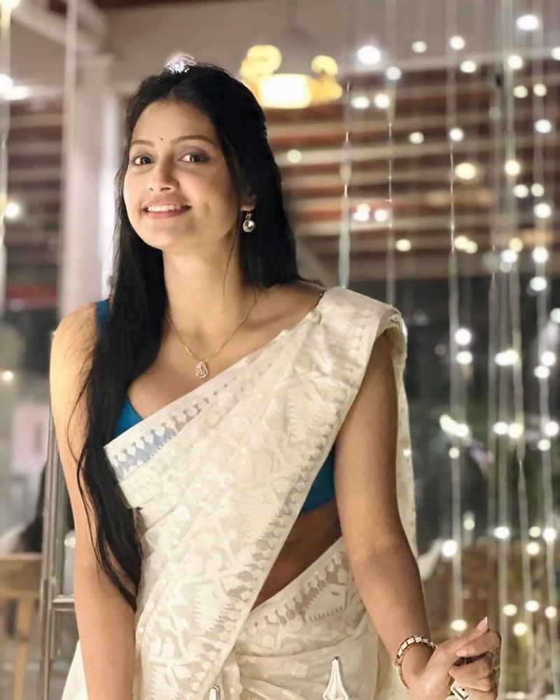 Debjani Modak in a cream and gold Bengali jamdani saree against a curtain of fairy lights