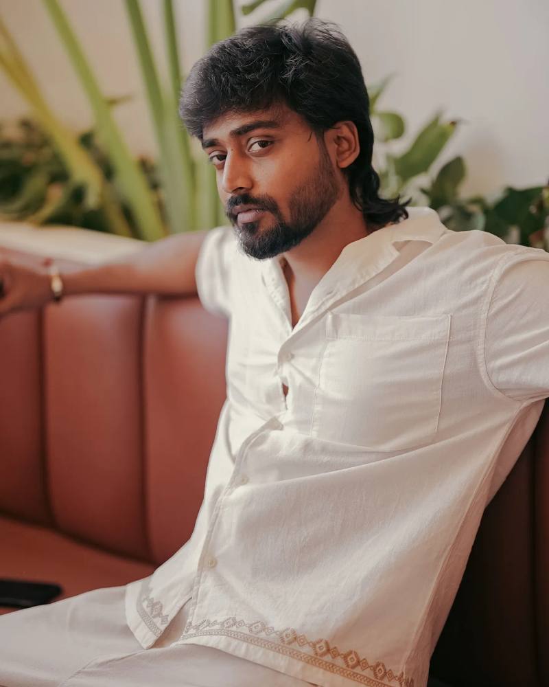 Mukesh Gowda in a white shirt on a leather sofa with plants behind him, from his own Instagram feed