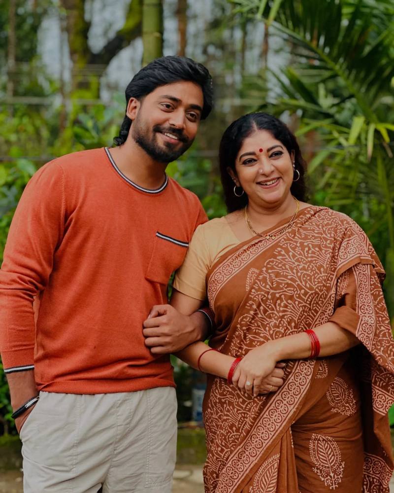 Mukesh Gowda in an orange sweater, photographed outdoors with a fellow actor