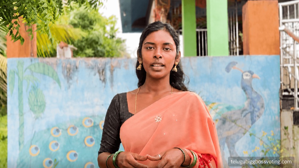 Illustrated portrait of Rajakumari Dayana in an orange saree in front of a peacock-mural wall in her village