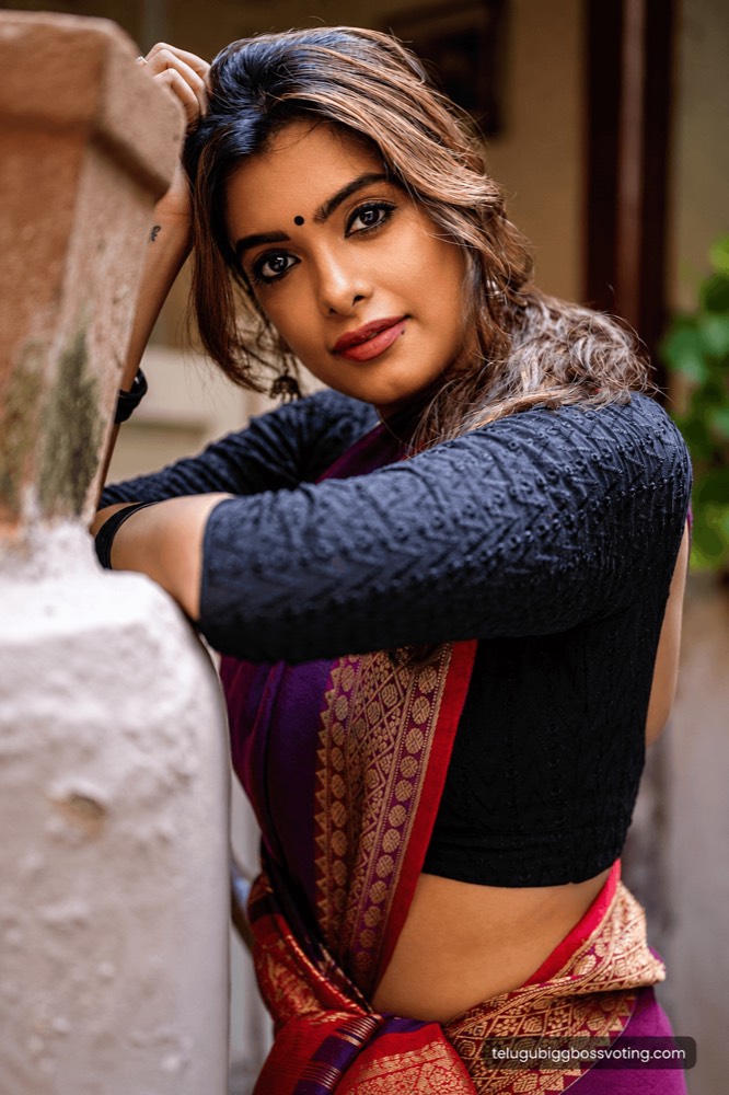 Illustrated close-up portrait of Srishti Vyakaranam in a maroon saree with a black blouse, leaning against a stone pillar