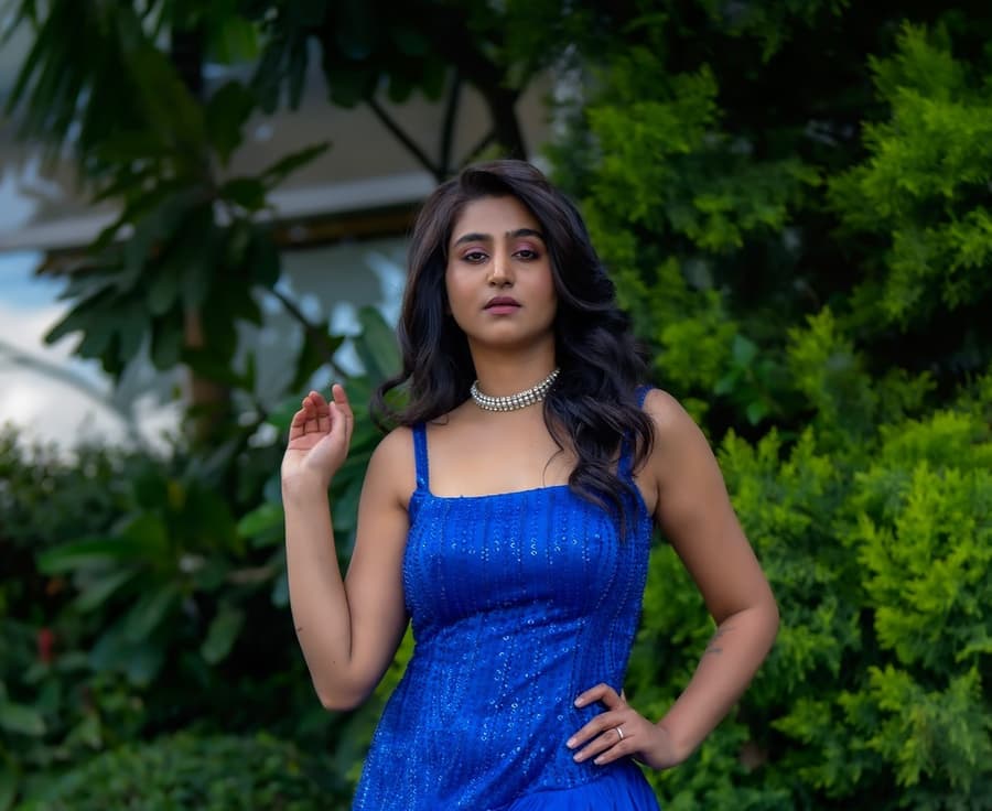 Varshini Sounderajan in a blue gown standing in front of greenery